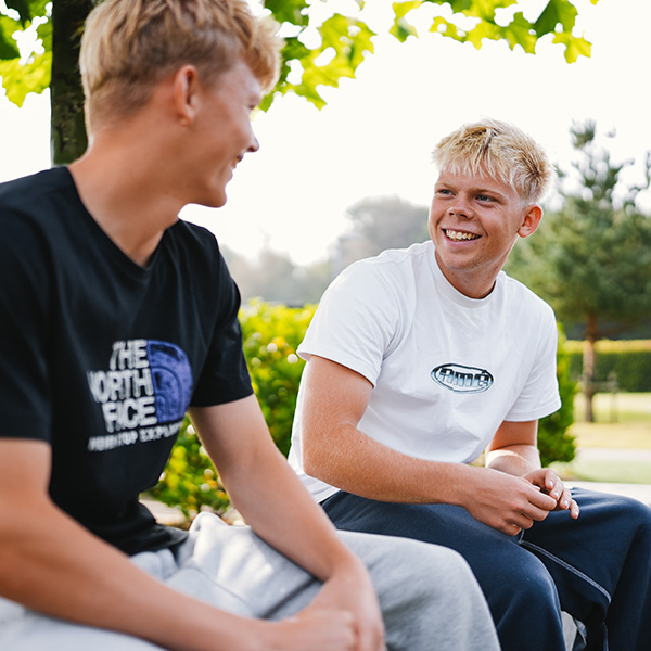 To unge drenge smiler og ser på hinanden udendørs på SINE