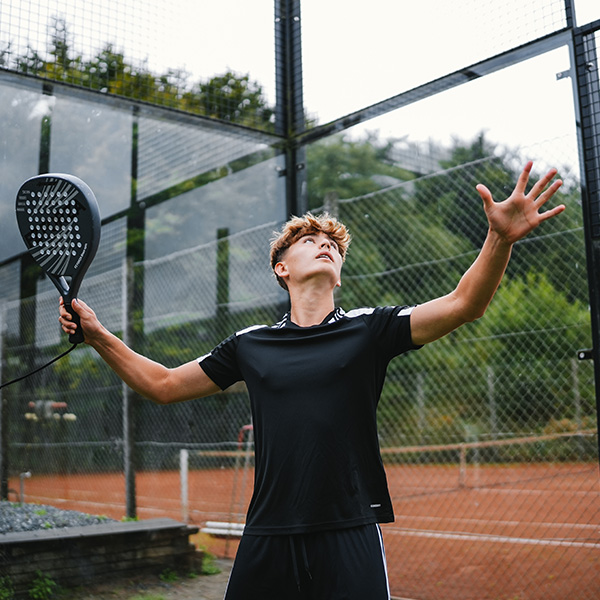 Ung mand i sort sportstøj og padelbat på en bane kigger op.